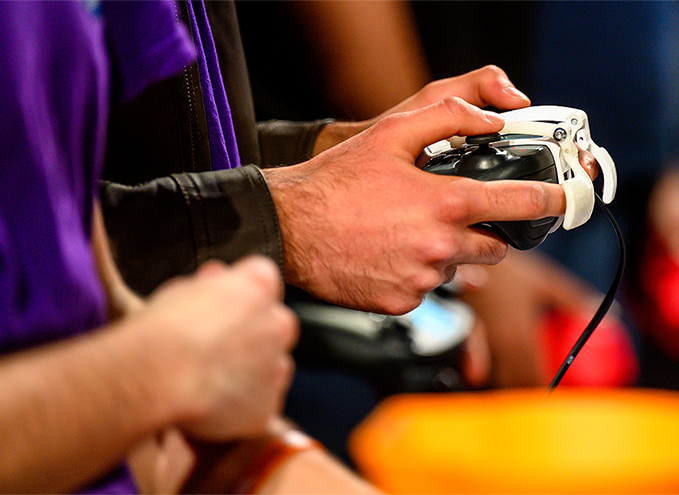 Close-up of hands holding a VEX Robotics controller with a wired connection during a competition.